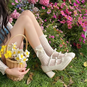 Close-up of white lace socks with silk bows and cream Mary Jane shoes on grass