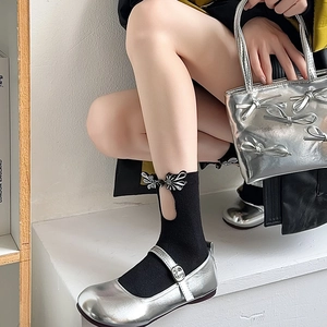 Detail of silver Mary Jane shoes with black mid-calf socks featuring Chinese knot buttons