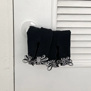 Detail view of black knit arm warmers with white floral buttons hanging on a door