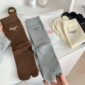 Detail of embroidered lettering on stylish tabi split-toe socks in various neutral tones