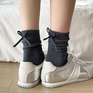 Detail of dark grey ribbed socks with black bow accents paired with vintage sneakers