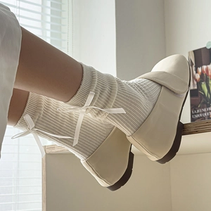 Detail of white ribbed crew socks with satin bow accent and cream Mary Jane flat shoes