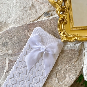 Detail of white hollow-knit calf socks featuring a silky satin bow in ballet style