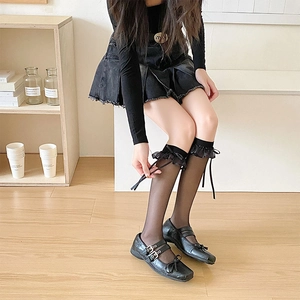 Détail de chaussettes hautes noires transparentes avec dentelle à volants et nœud en ruban