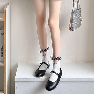 Detail of white mid-tube socks with bow ornament and cutout paired with Mary Jane shoes