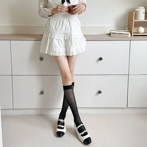 Detail of black fine mesh knee-high socks paired with Mary Jane shoes in a minimalist setting