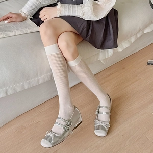 Detail of white mesh knee high socks paired with silver Mary Jane shoes and bows