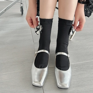 Detail of black knit socks with bow decor paired with silver Mary Jane shoes