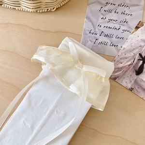Close-up of white lace calf socks with yellow organza ruffles and silk bow detailing