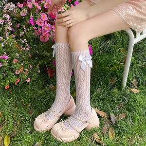 Detail of pink bow Mary Jane shoes paired with white lace mid-calf socks on grass