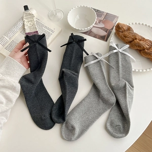 Detail of ribbed knit socks with silk bows on a white table with lifestyle props