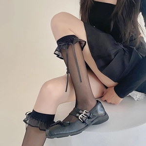 Détail de chaussettes hautes noires transparentes avec bordures à volants et petits nœuds