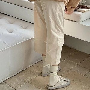 Detail of beige wide-leg trousers styled with white lettered socks and canvas mule shoes