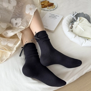 Detail of black ribbed knit socks featuring a delicate bow tie on the side cuff