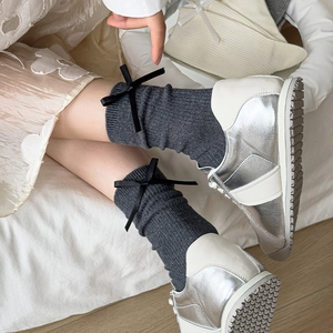 Detail of dark grey knit mid-calf socks with black ribbon bow and silver sneakers