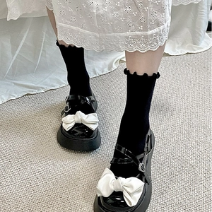 Détail de Mary Janes en cuir verni noir avec nœud blanc et brides croisées
