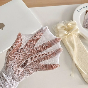 Close-up of white hollow lace socks with satin bows and intricate heart mesh patterns