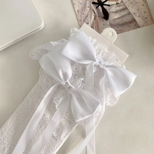 Detail of white lace socks featuring large satin bows and delicate floral embroidery