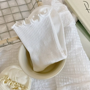 Détail de chaussettes blanches à volants avec texture côtelée dans un bol de couleur crème