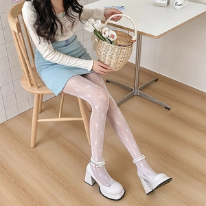 Detailed view of white heart pattern fishnet tights on model in a cozy indoor setting