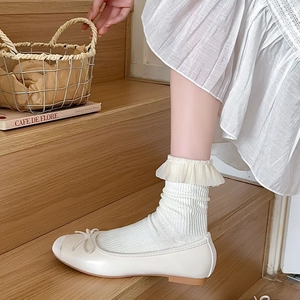 Detailansicht cremefarbener Ballerinas mit Schleifen und Socken mit Spitzenvolants