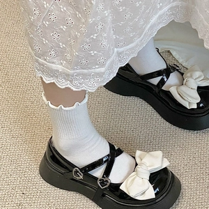 Détail de Mary Janes noires à plateforme avec boucle cœur et nœud crème décoratif