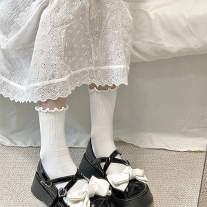 Détail de babies à plateforme noires avec nœuds blancs et boucles en cœur sur chaussettes