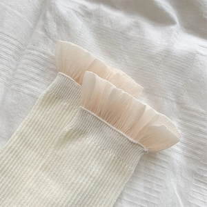 Nahaufnahme cremeweißer Rippsocken mit mehrlagigen Rüschen aus transparentem Tüll