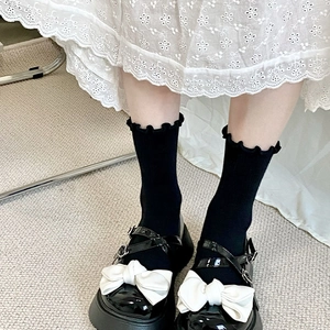 Chaussettes noires à froufrous avec chaussures Mary Jane vernies et nœuds blancs