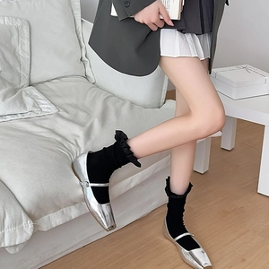 Detail von silbernen Mary Jane Schuhen mit schwarzen Rüschensocken im gemütlichen Look