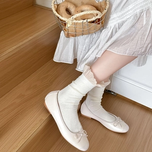 Detailansicht von cremefarbenen Ballerinas mit Schleife und passenden Socken mit Spitzenrand