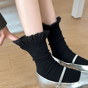 Detail von schwarzen Rüschensocken kombiniert mit silbernen Mary-Jane-Schuhen auf Holz