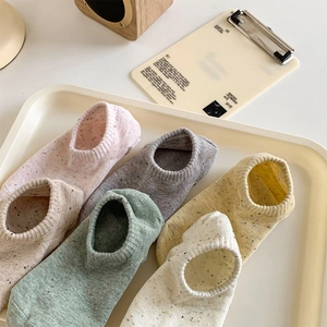 Close-up of six colorful flecked knit ankle socks arranged neatly on a cream display tray