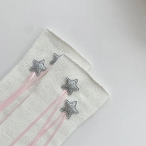 Detail of white ribbed knit leg warmer with silver glitter stars and pink silk ribbons