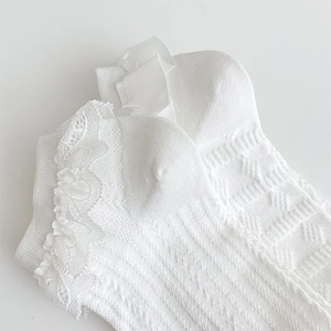 Détail de chaussettes Lolita blanches avec nœuds satin, dentelle et texture tricotée ajourée