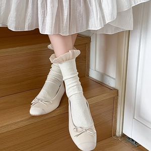Detail von cremeweißen Strick-Wadenstrümpfen mit Rüschen und beigen Ballerinas