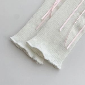 Macro detail of white ribbed knit leg warmers with delicate light pink satin ribbons