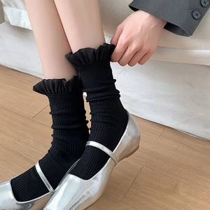 Detail von schwarzen Socken mit Rüschenrand kombiniert mit silbernen Mary-Jane-Schuhen