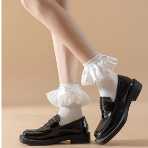 Detail of white ruffle socks with satin lace layers worn with black patent leather loafers