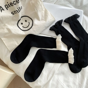 Nahaufnahme schwarzer Socken mit Spitzenbesatz und Netzrüschen auf weißem Betthintergrund