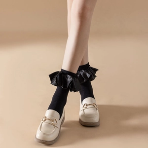 Close-up of black frilly ribbon socks paired with beige loafers featuring horsebit detail