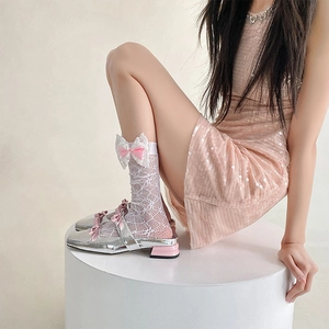 Detail of white lace mesh socks featuring a large pink bow and silver Mary Jane shoes