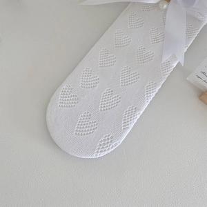 Détail du motif en maille de cœur avec nœud en soie et perle sur chaussettes blanches