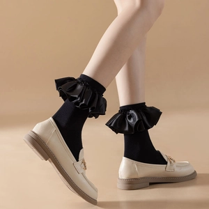 Detail of black mid-calf socks with satin ruffle lace trim paired with retro loafers