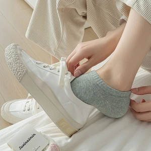 Detail of grey low-cut cotton socks worn with white canvas sneakers on wooden floor