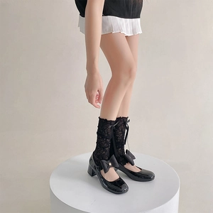 Detail of black Mary Jane shoes with bows and lace leg warmers on a white pedestal