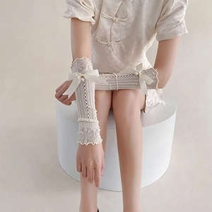 Close-up of white lace arm sleeves with satin bows and pearl charms for a balletcore style