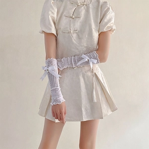 Close-up of white lace sleeve featuring ruffle trim, mesh texture, and a satin bow with pearl