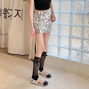 Détail de jambières en résille blanche avec nœuds et mini-jupe à paillettes argentées