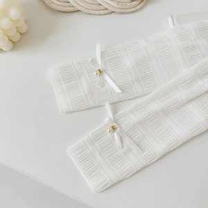 Detailed close-up of white pleated leg warmers with delicate silk bows and pearl accents